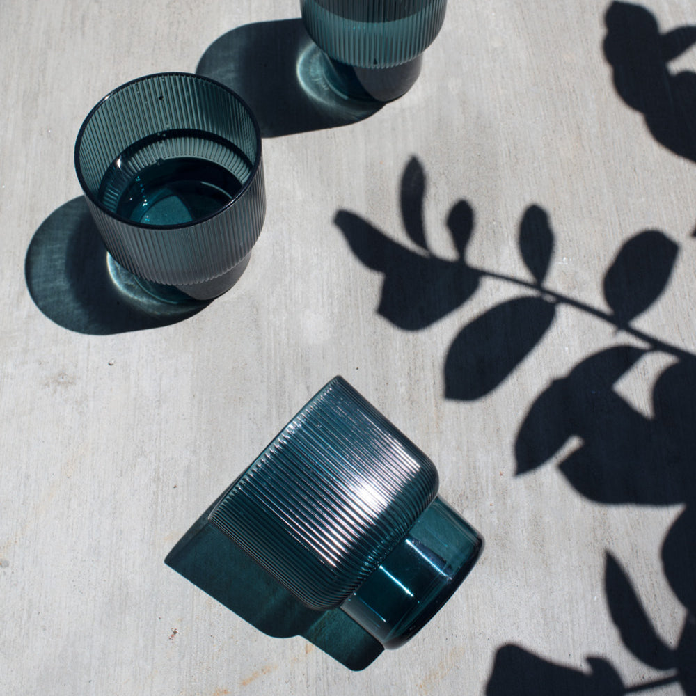 Blue glasses filled with water and shadows of some leaves on the table