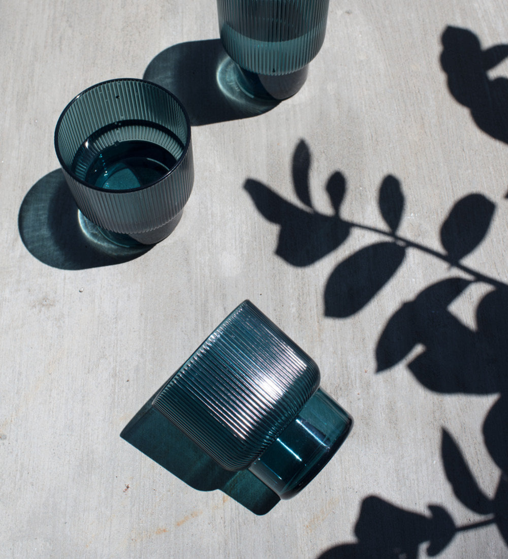 Blue glasses filled with water and shadows of some leaves on the table